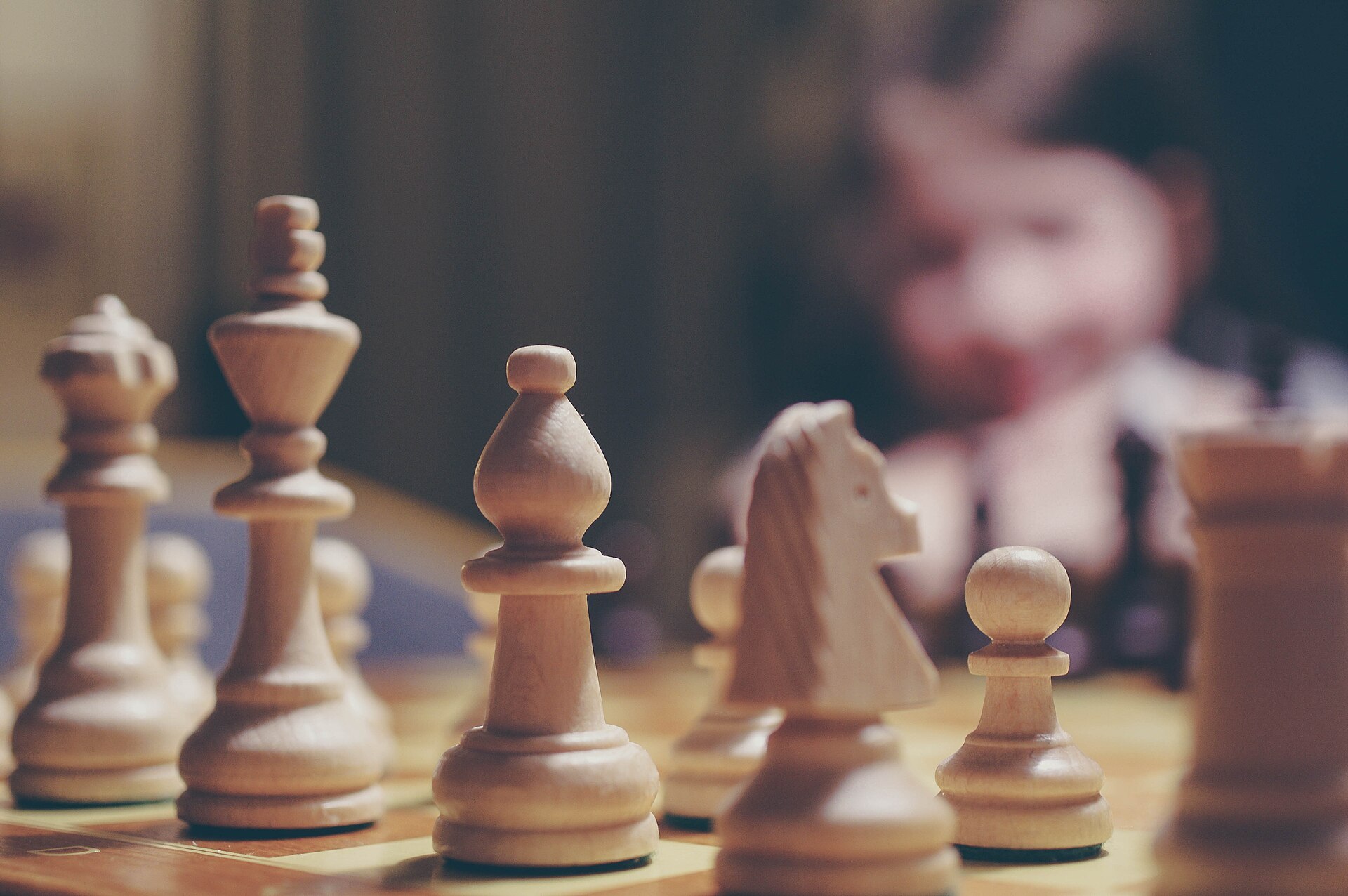 Wooden chess pieces on a board with a young player behind them